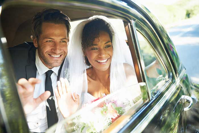 newlywed couple looking out the window of a car and waving