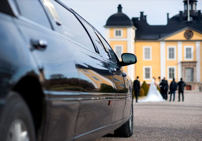 Black limo waiting for bride and groom in front of mansion. 