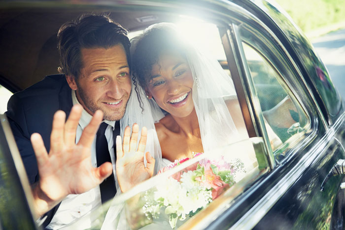 newlywed couple looking out the window of a car and waving