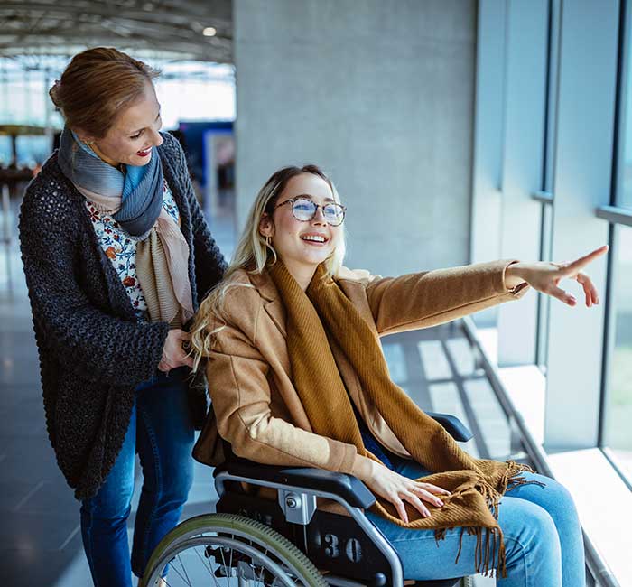 Young disabled woman on wheelchair and carer waiting at airport and looking at window view