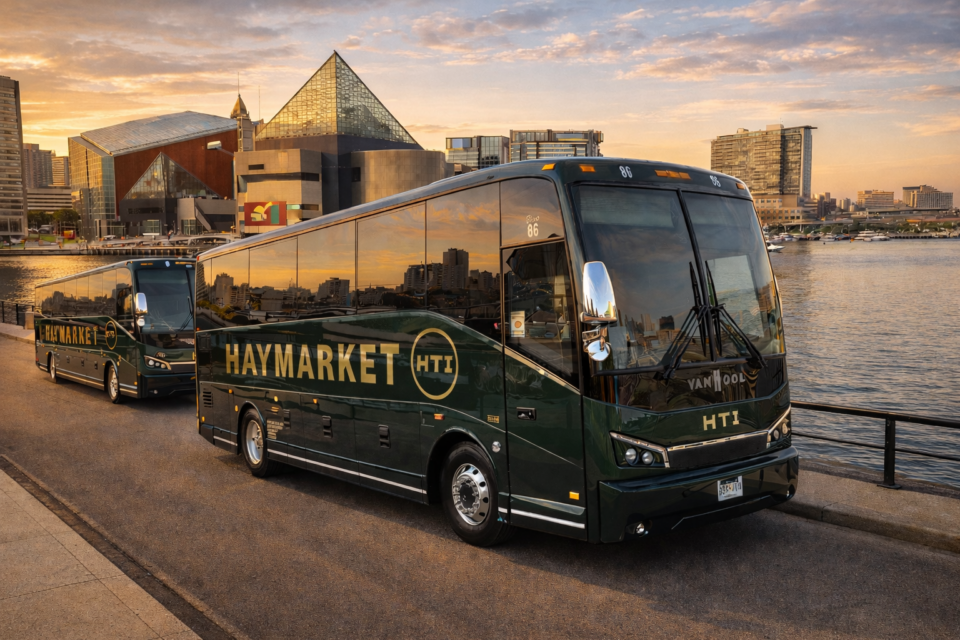 Two dark green Haymarket Transportation Inc. luxury minibuses at Baltimore Inner Harbor during golden hour near the National Aquarium.